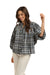 Italian Star Women's Freida Check Shirt. Woman wearing a blue plaid shirt and white pants standing against a stone wall.
