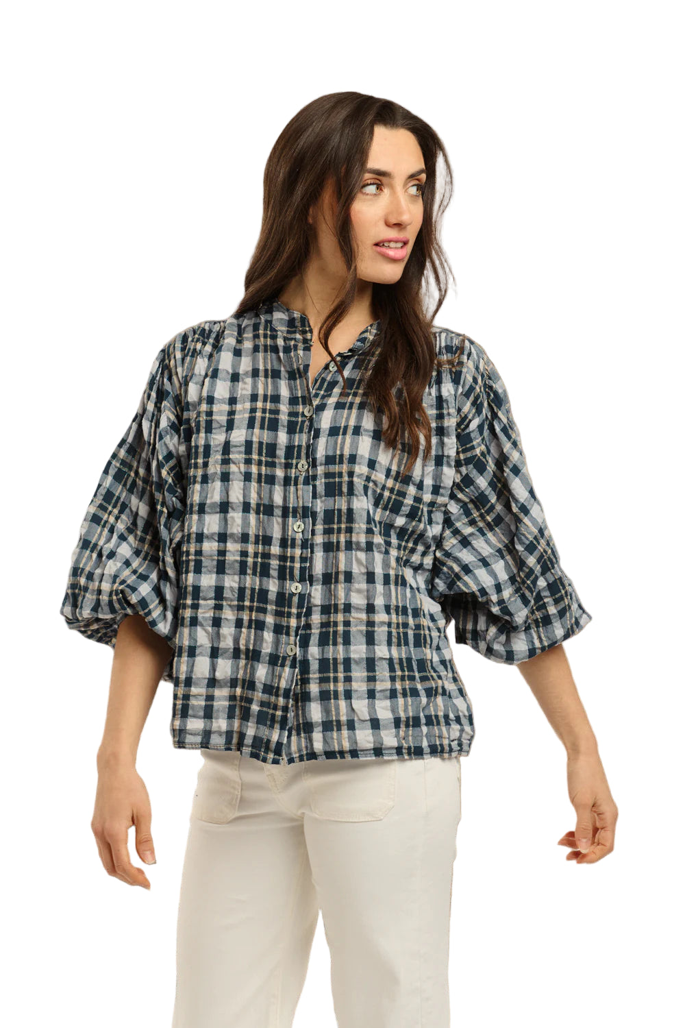 Italian Star Women's Freida Check Shirt. Woman wearing a blue plaid shirt and white pants standing against a stone wall.