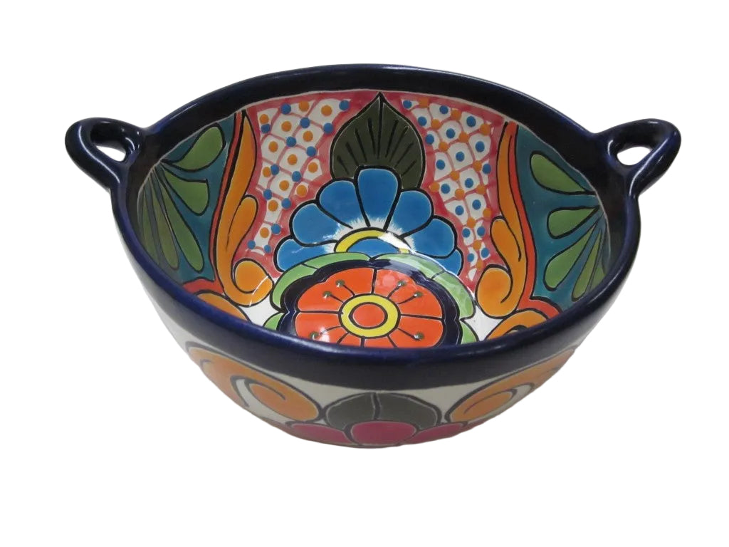 A hand-painted ceramic bowl with two side handles, featuring a vibrant Mexican Talavera style design with a central blue flower and orange, green, and yellow patterns on a white background.