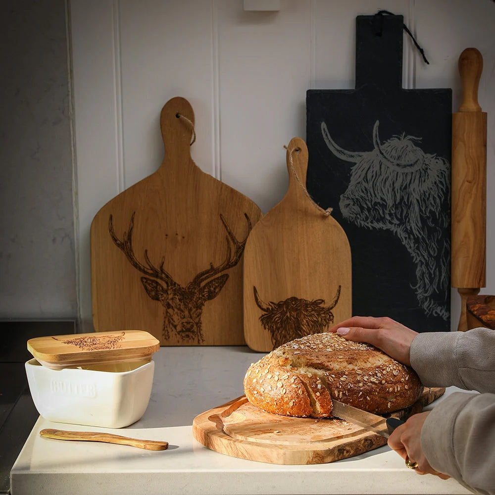 Wooden cutting boards with animal designs on a kitchen counter with bread and a person's hand.