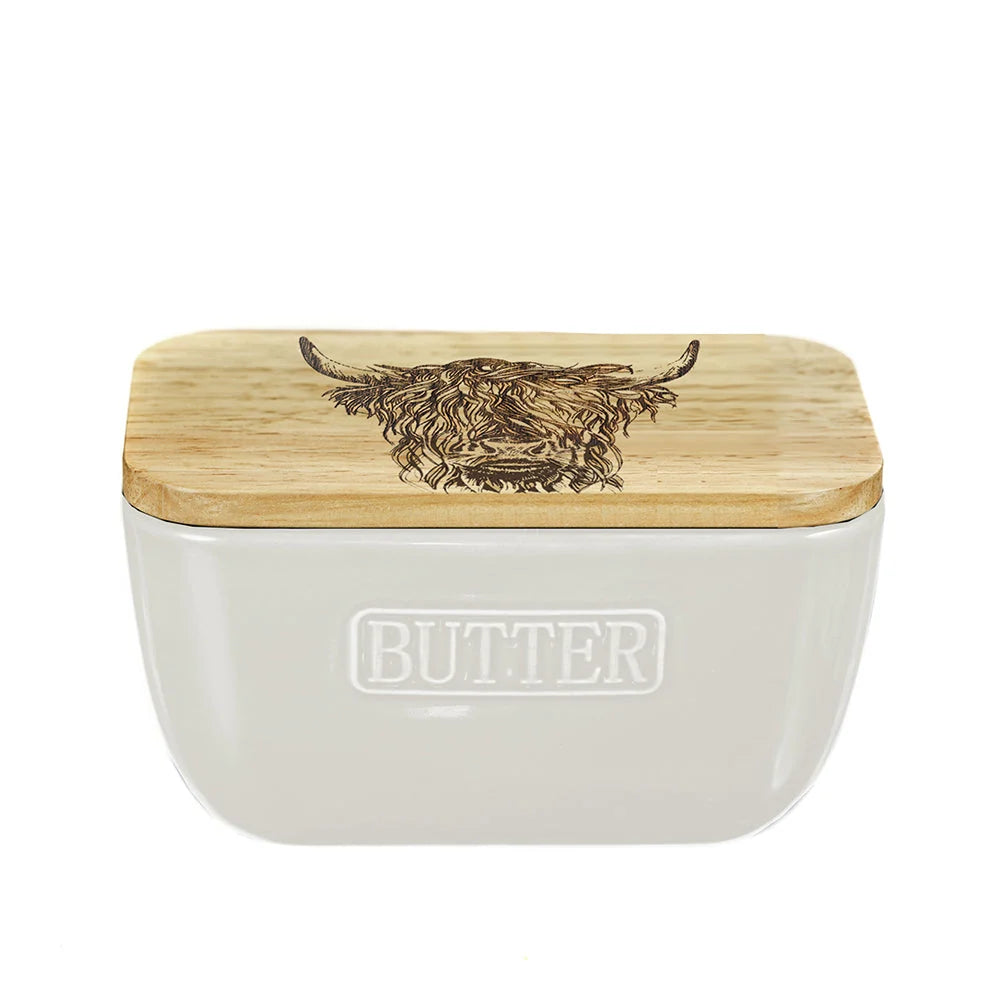 A white ceramic butter container with a light natural wood lid featuring a dark engraved Highland cow design. The word 'BUTTER' is embossed on the front of the container.