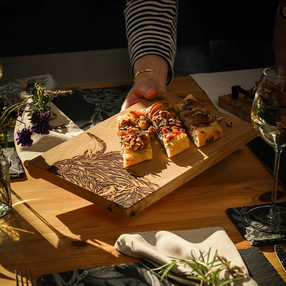 Wooden cutting board with sliced pizza on a table with wine glass and flowers.