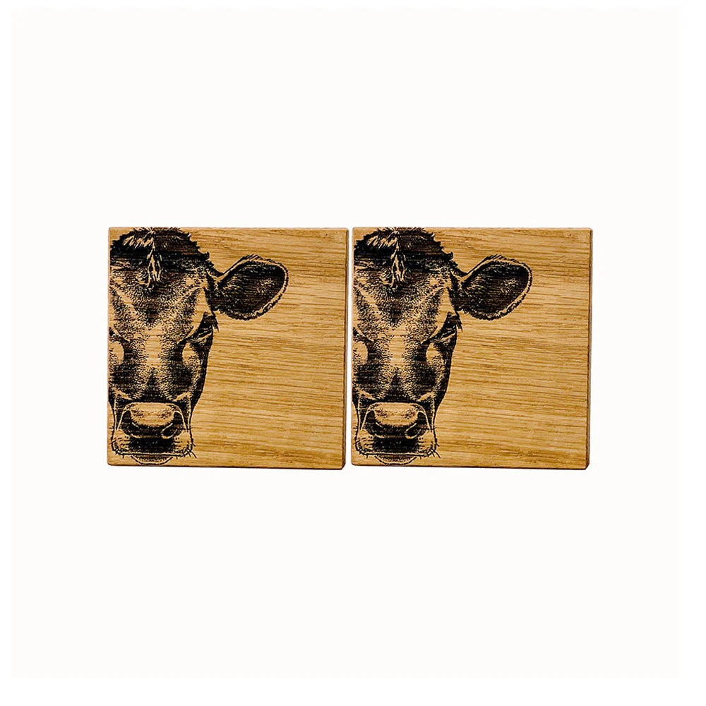 Two square wooden coasters featuring a detailed black engraving of a cow's face on a light brown wood grain background, displayed side-by-side on a white background.