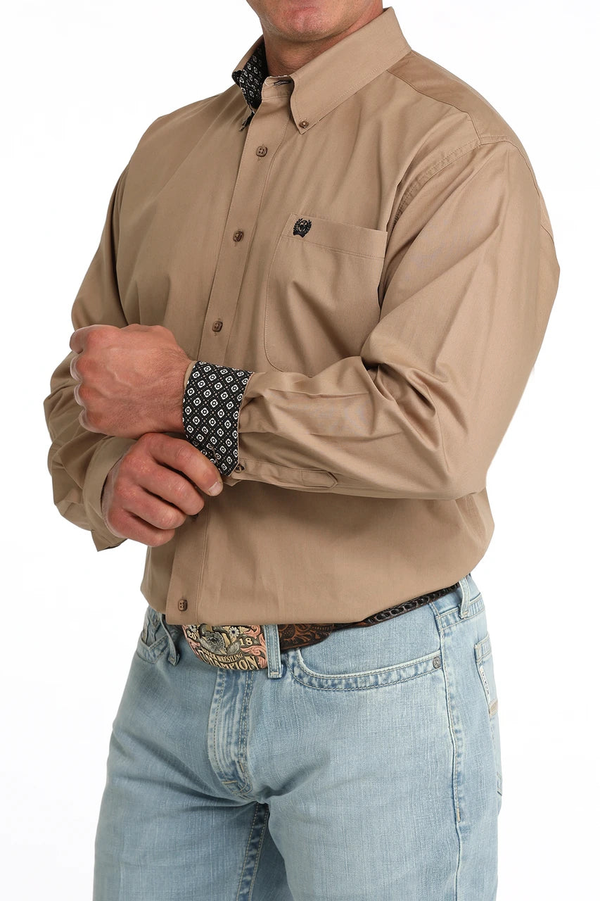 Man wearing a beige long-sleeve shirt and light blue jeans on a white background