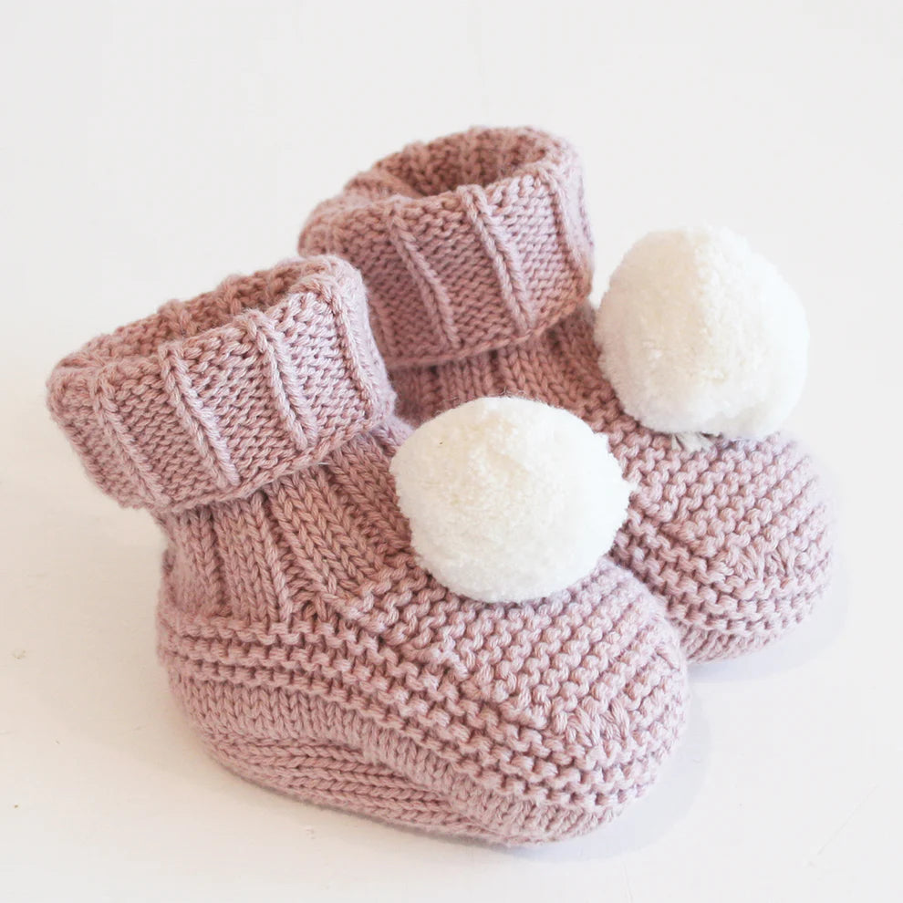 Knitted baby booties with white pom-poms on a light background