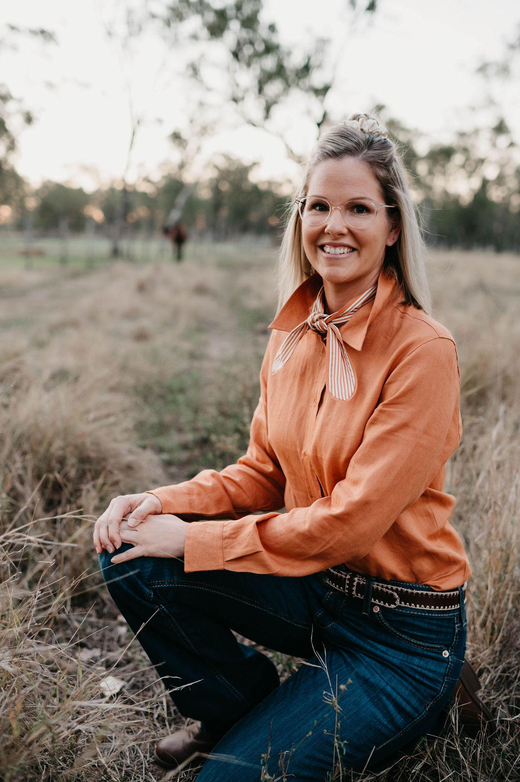 Kitty Fordè Camilla Plain Linen L/S Shirt. Woman in an orange blouse and blue jeans sitting in a field.