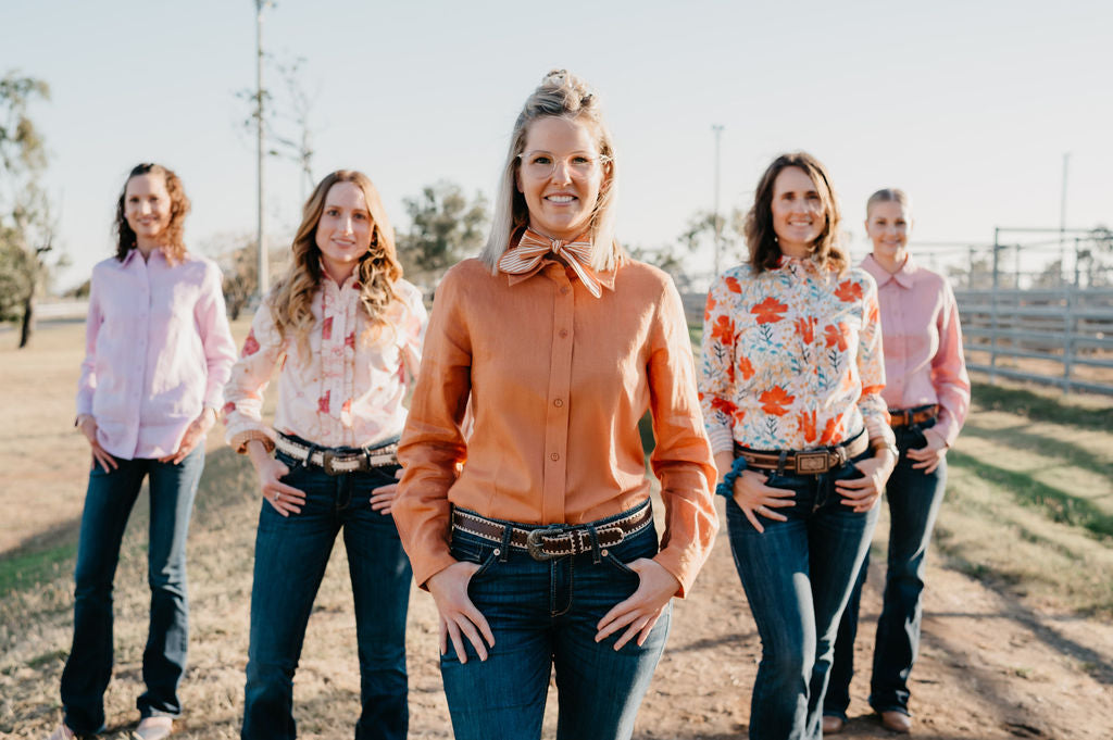 Five women standing on a dirt road with a clear sky background