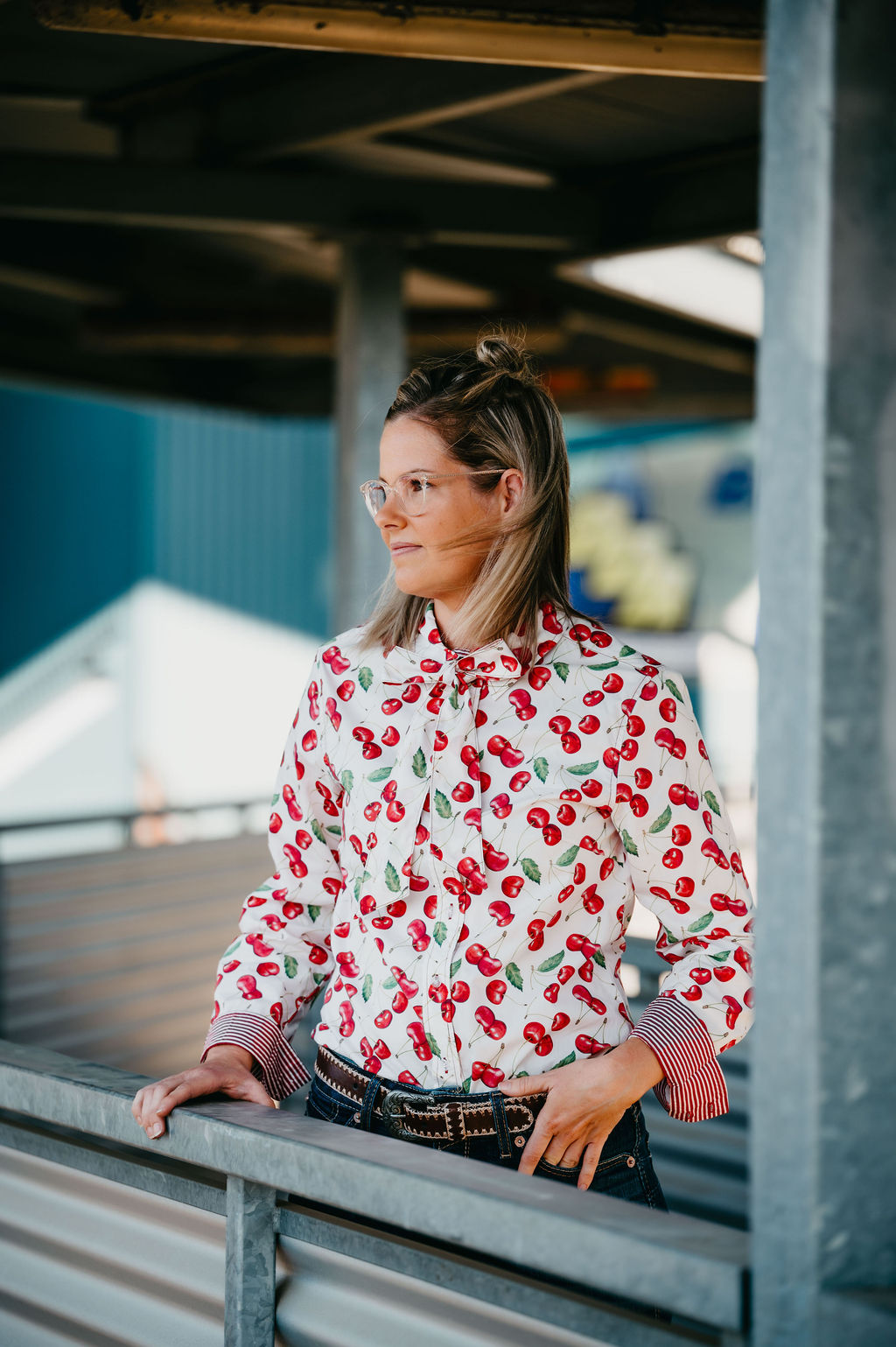 Woman wearing a red and white patterned shirt standing under a bridge.