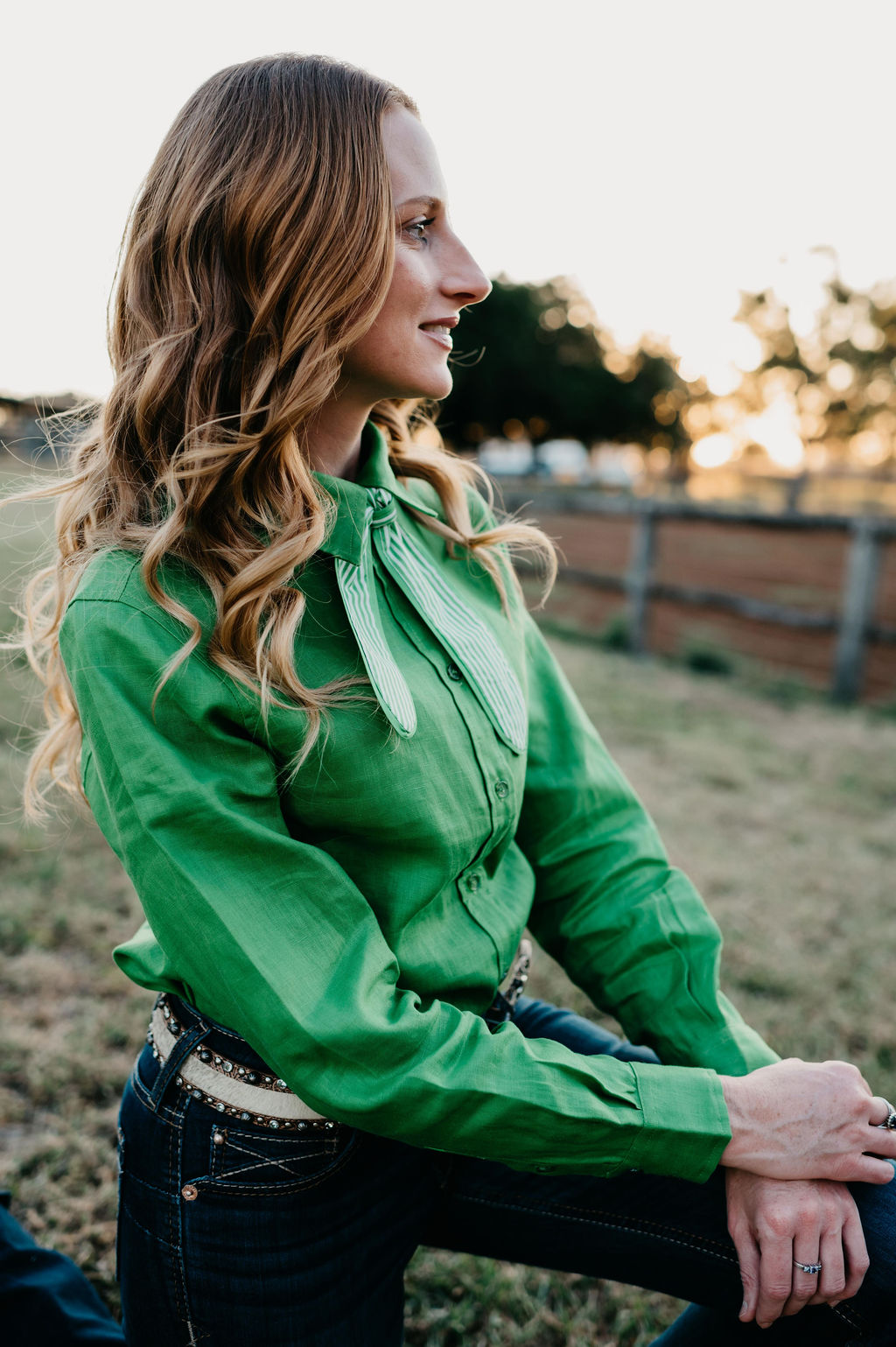 Woman wearing a green blouse with a bow tie sitting outdoors.