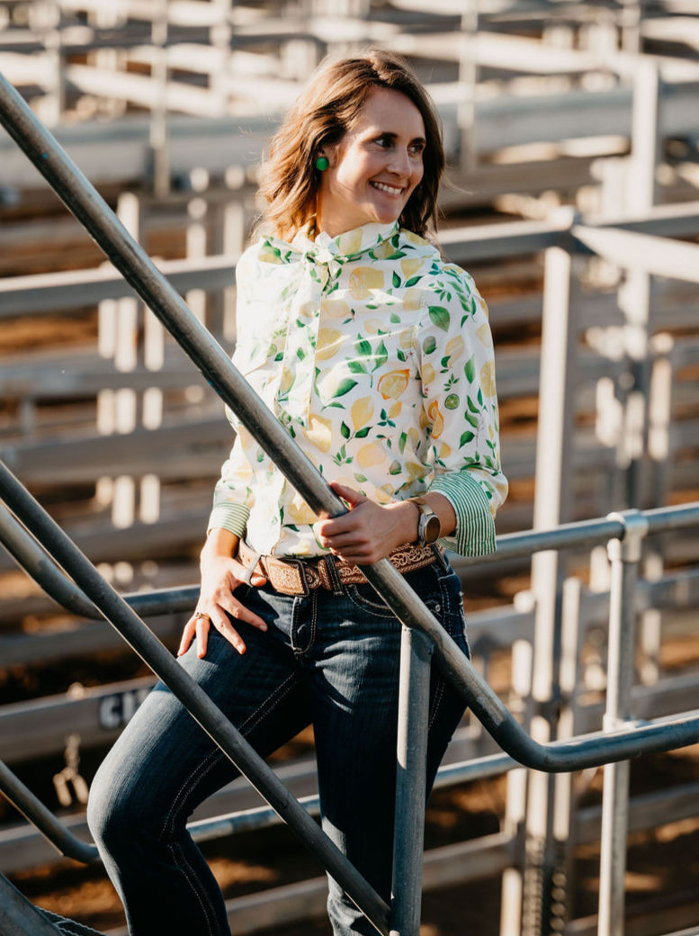 Kitty Fordè Kerrie Printed L/S Shirt. Woman standing on metal bleachers wearing a patterned shirt and jeans.