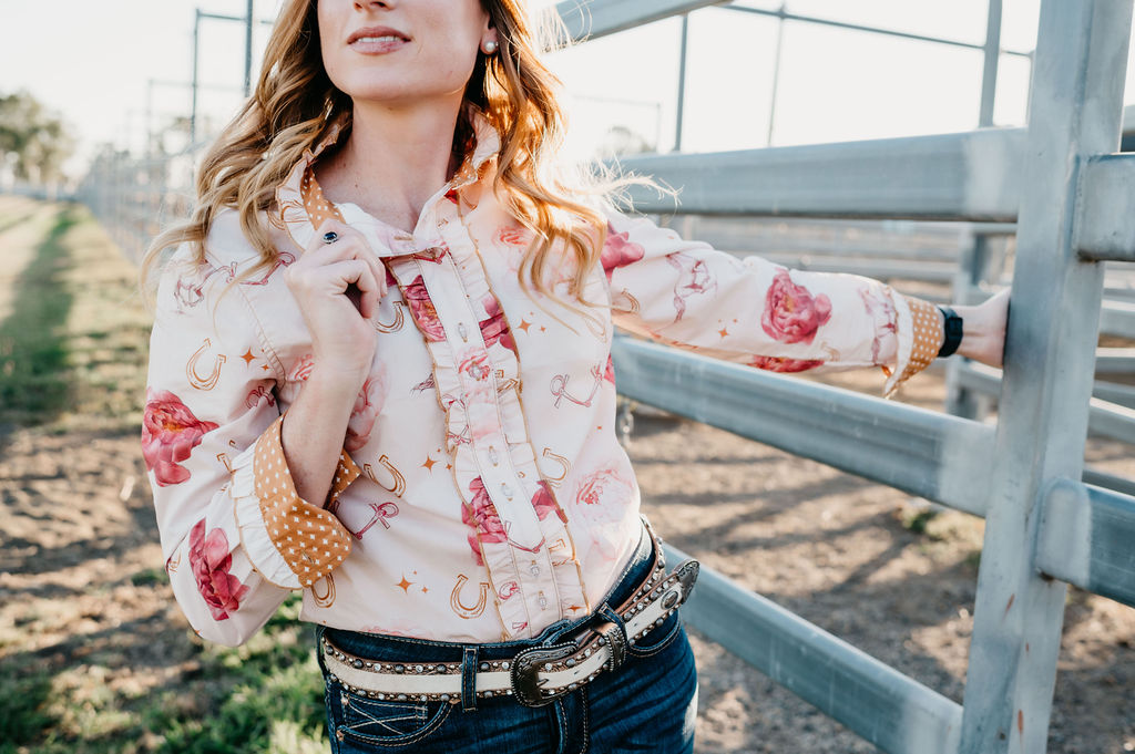 Woman wearing a floral shirt and jeans standing near a metal fence.