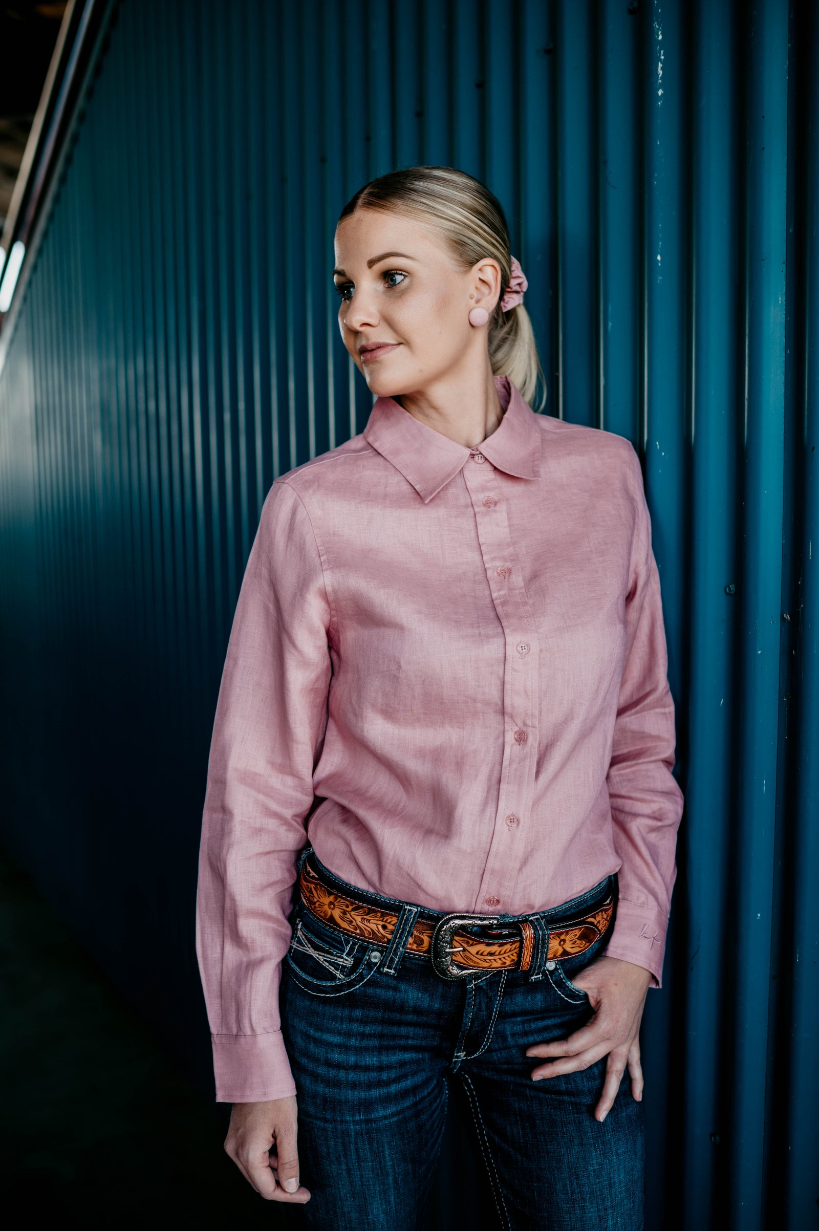 Woman wearing a pink shirt and blue jeans against a dark background