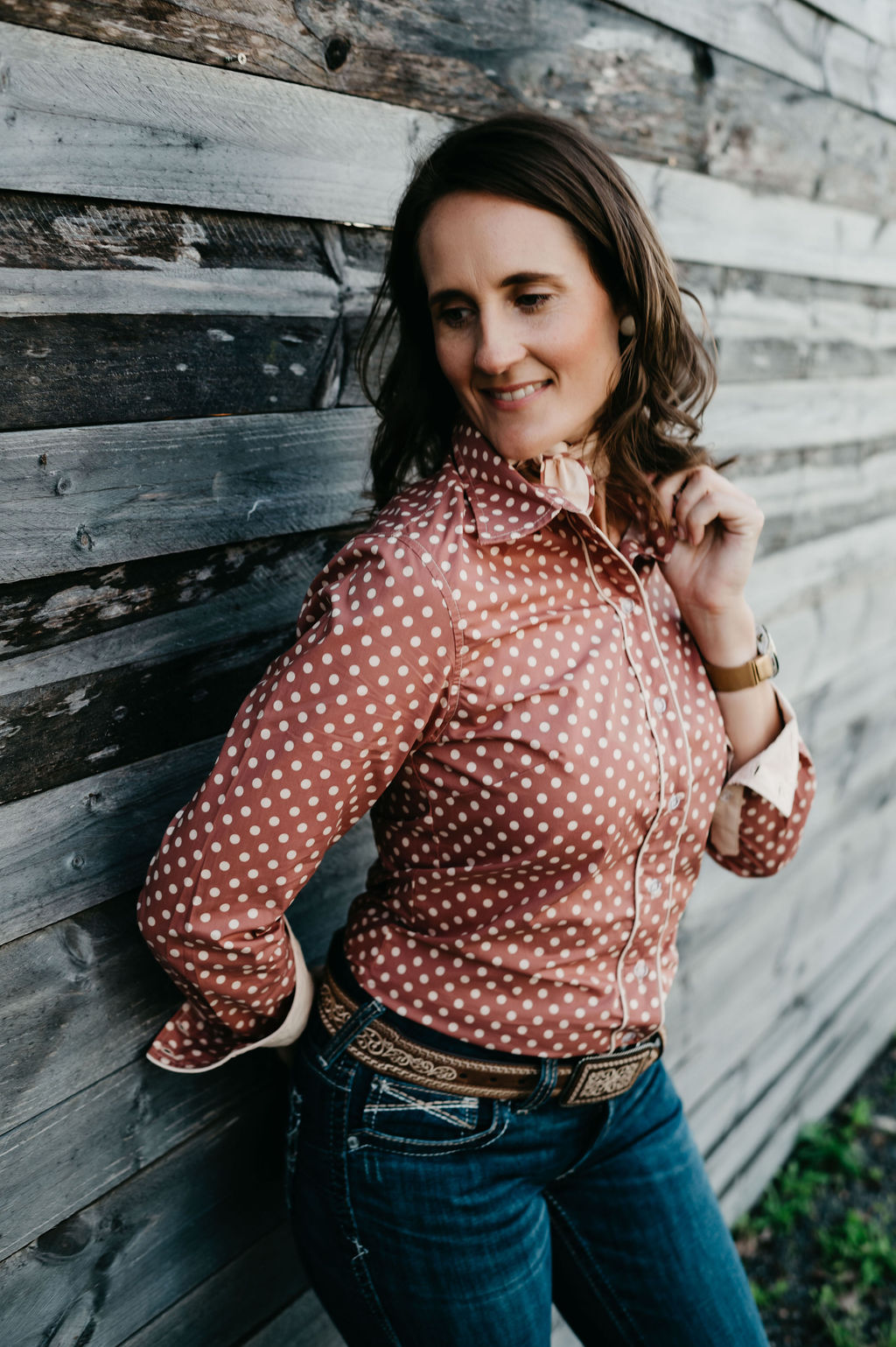 Kitty Fordè Petrina Printed L/S Shirt. Woman wearing a brown polka dot blouse and jeans against a wooden wall.