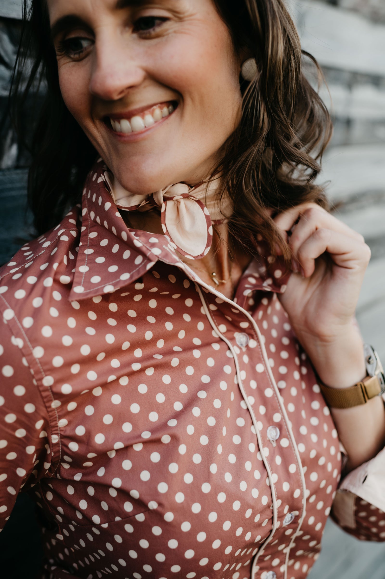 Woman wearing a polka dot blouse with a scarf, smiling outdoors.