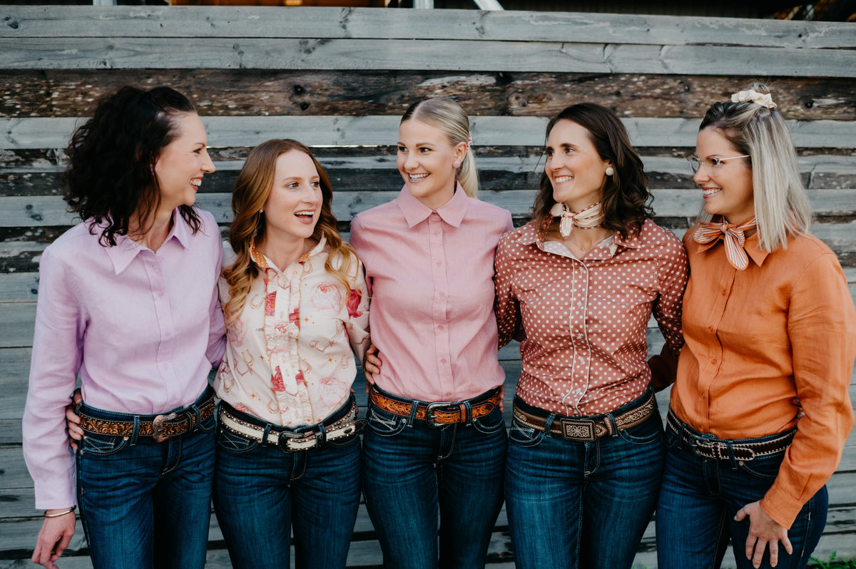 Five women standing together on a wooden bench, smiling and posing for a photo.