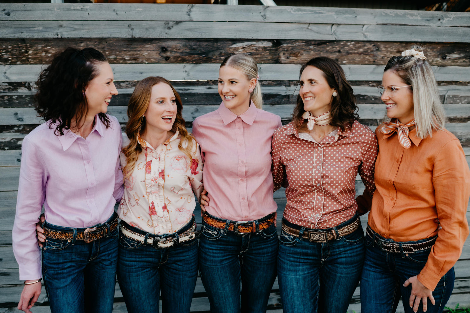 Five women standing together on a wooden bench, smiling and posing for a photo.