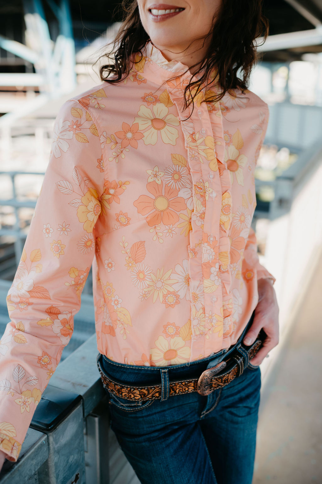 Kitty Fordè Stace Printed L/S Shirt. Person wearing a pink floral blouse with jeans, standing on a bridge.