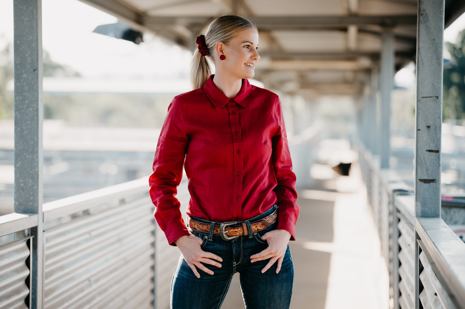 Woman wearing a red shirt and blue jeans standing on a metal platform.