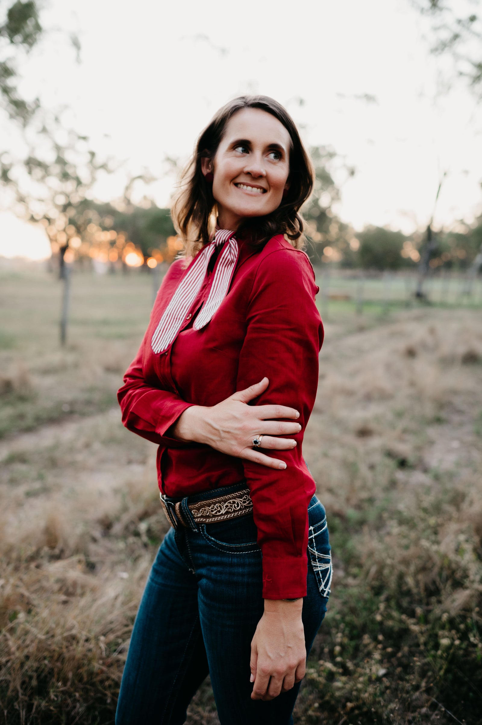 Kitty Fordè Tanielle Plain Linen L/S Shirt. Woman in a red shirt and blue jeans standing in a field with trees in the background