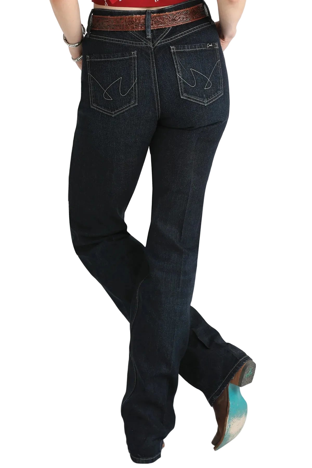 Cruel Denim dark wash denim jeans with a distinctive wing logo patch on the back pocket, shown on a model from the back wearing a brown western belt and cowboy boots.