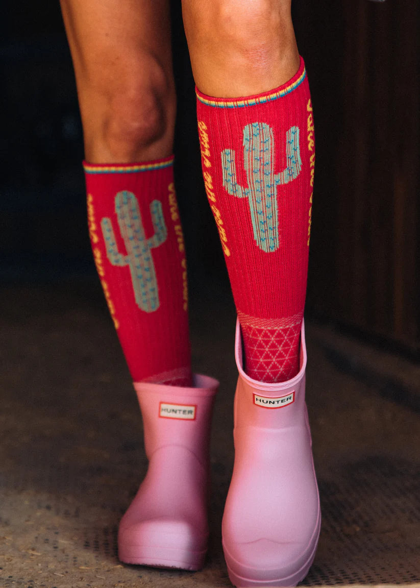 Lucky Chuck Take the Risk Performance Socks. Pink Hunter boots with red socks featuring cactus designs on a dark background