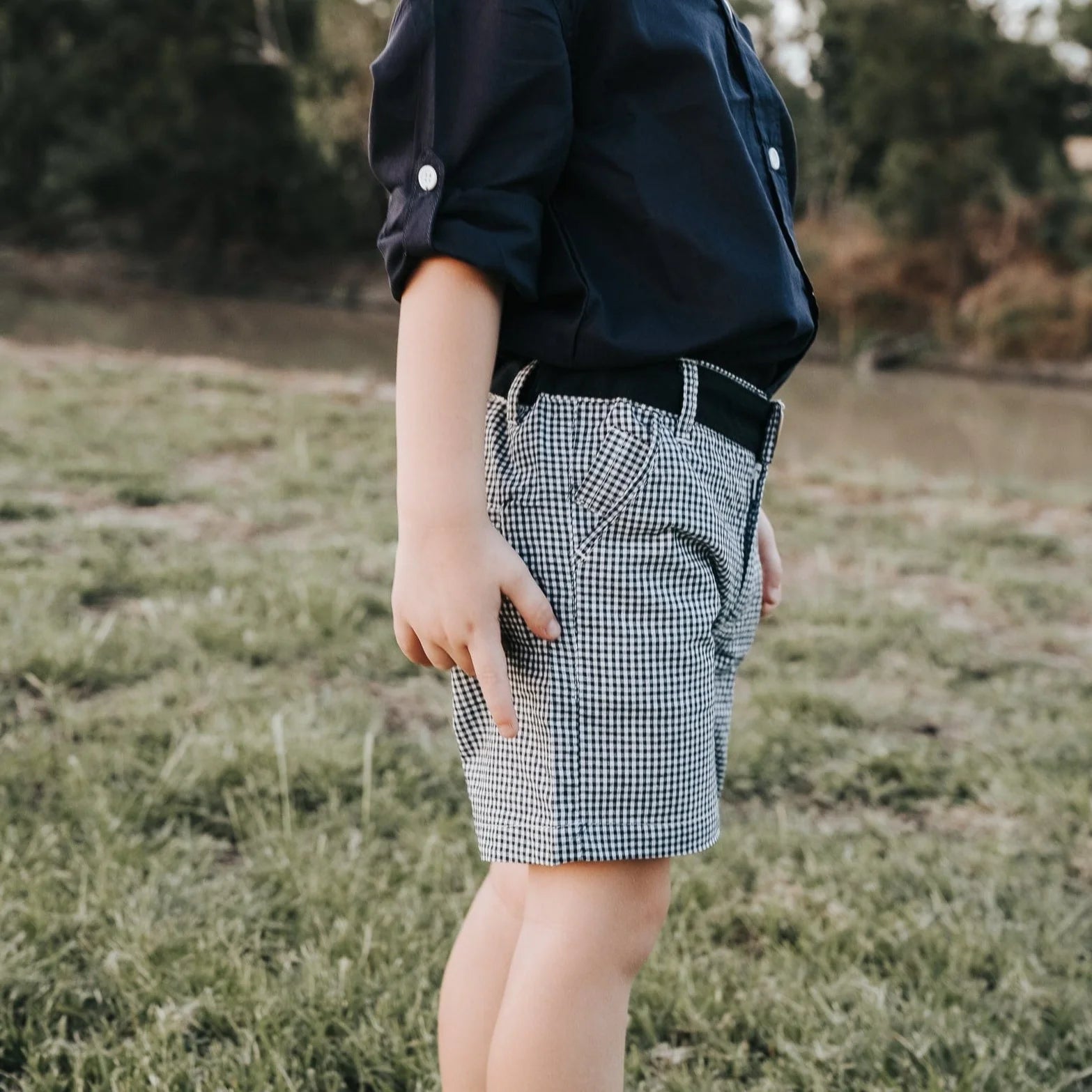 Love Henry Boy's Oscar Shorts. Navy gingham checkered shorts with a functional button fastening at the front and a decorative button on the right back pocket, featuring an elasticated waistband.
