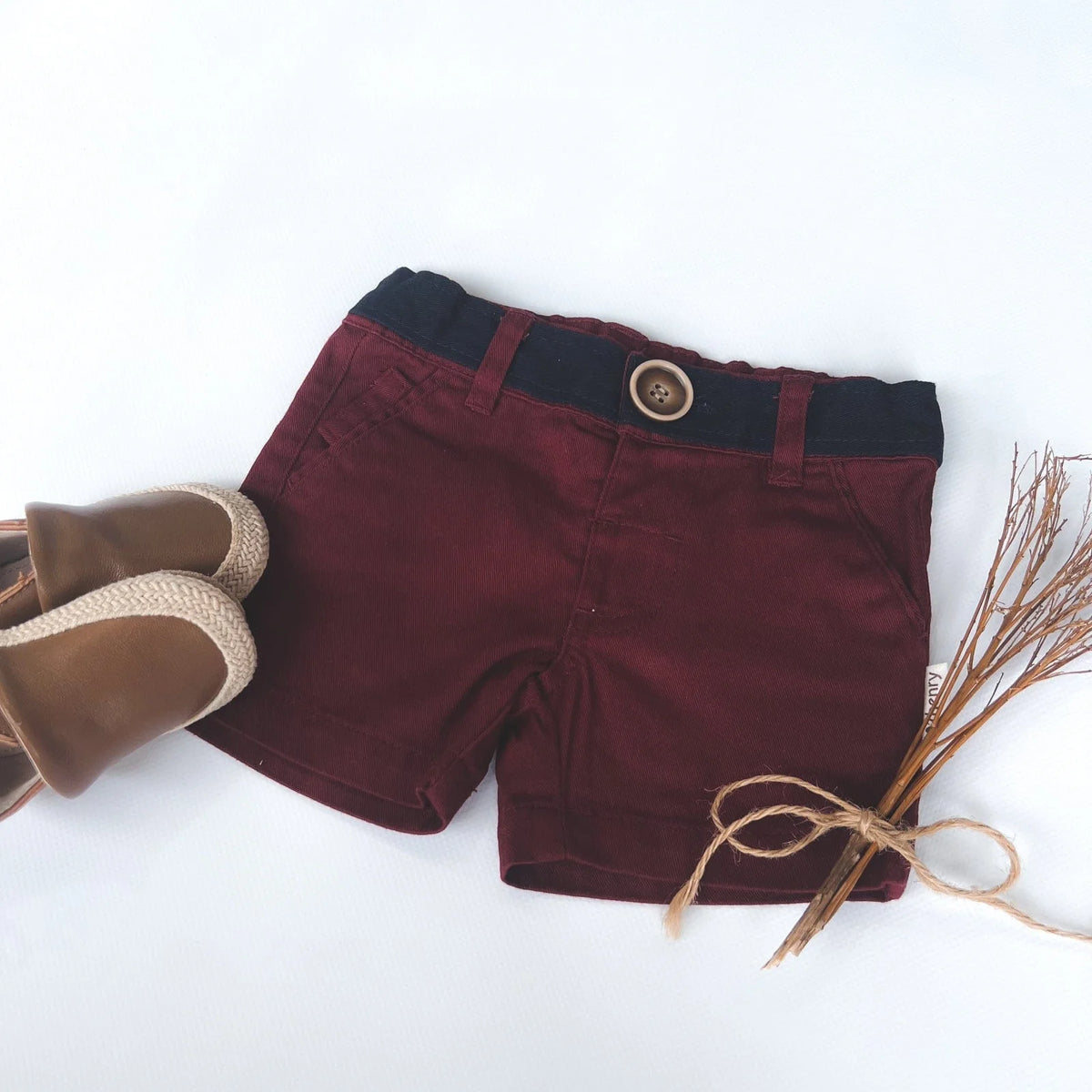 Love Henry Infant Boy's Oscar Shorts. A pair of maroon infant boy's shorts with a belt, button fastening, and pockets, accompanied by a pair of brown shoes.