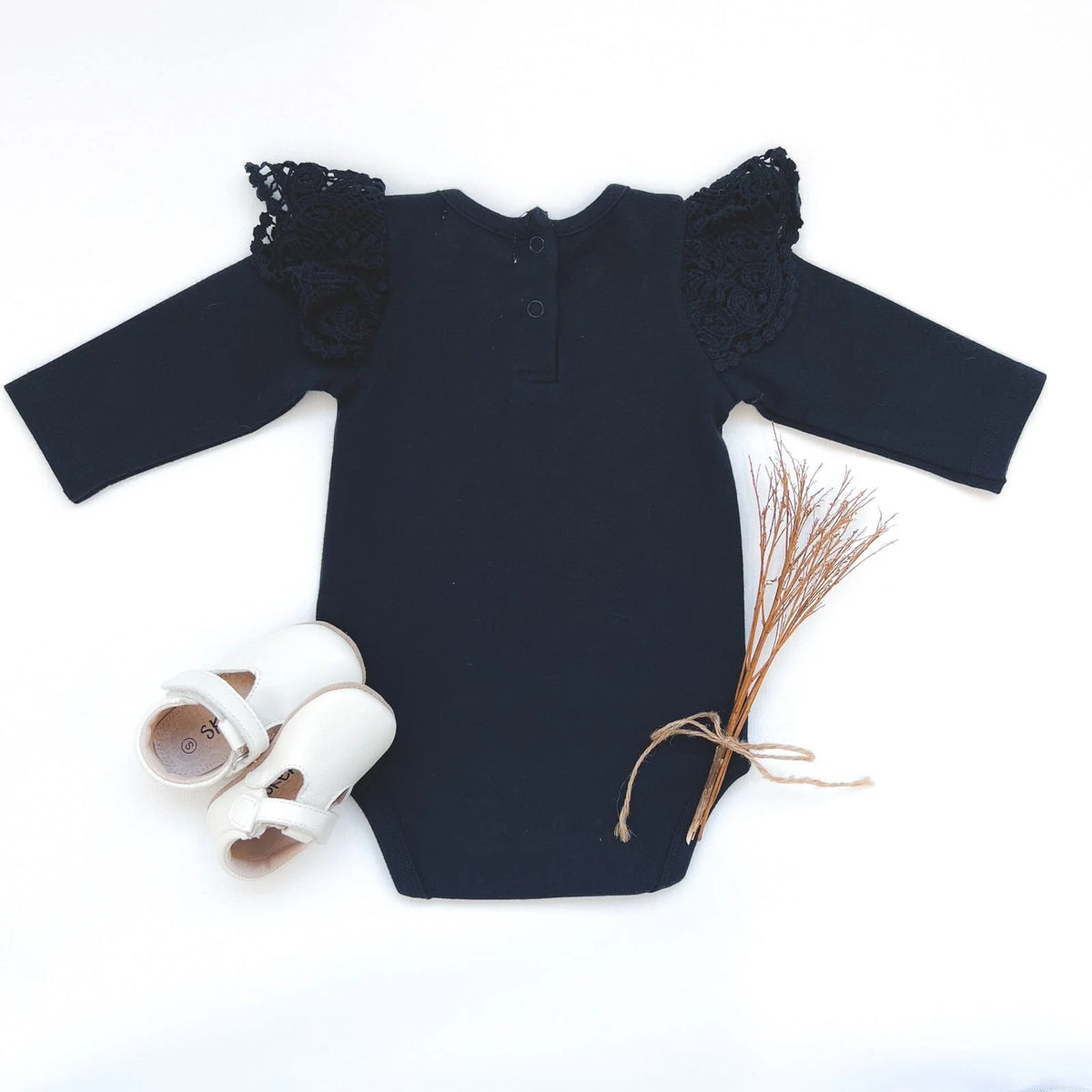 Love Henry Baby Girl's Lace Sleeve Onesie. Navy baby onesie with lace sleeves and a bias bound crew neck, accompanied by a pair of white shoes and a decorative element.