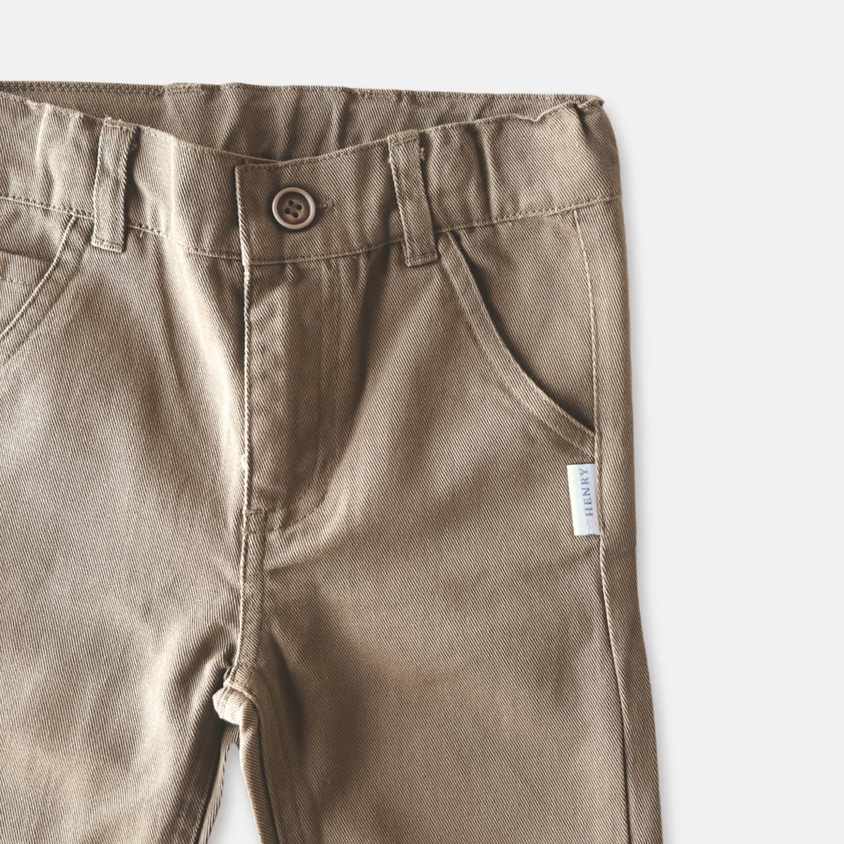 Love Henry Boy's Chino Pants. Close-up of brown pants with a button and label on a plain background.