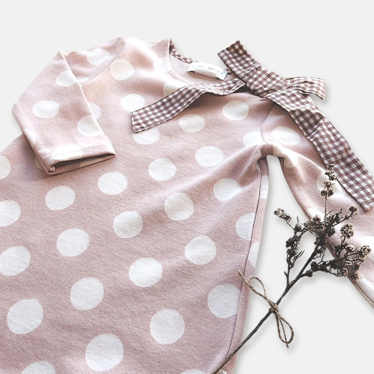 Love Henry Girl's Mary Dress. Pink polka dot dress with a checkered bow and dried flowers on a light background.