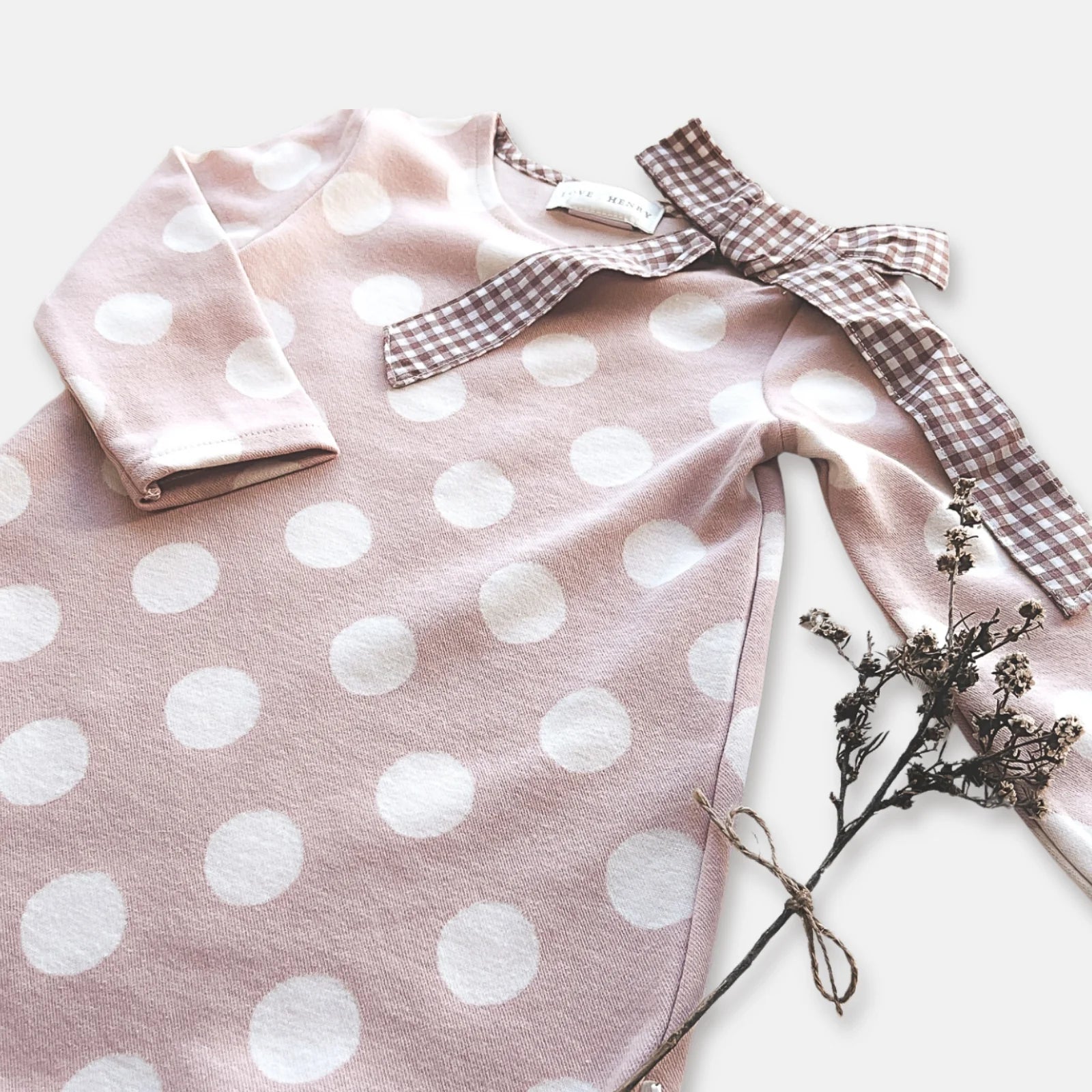 Love Henry Girl's Mary Dress. Pink polka dot dress with a checkered bow and dried flowers on a light background.