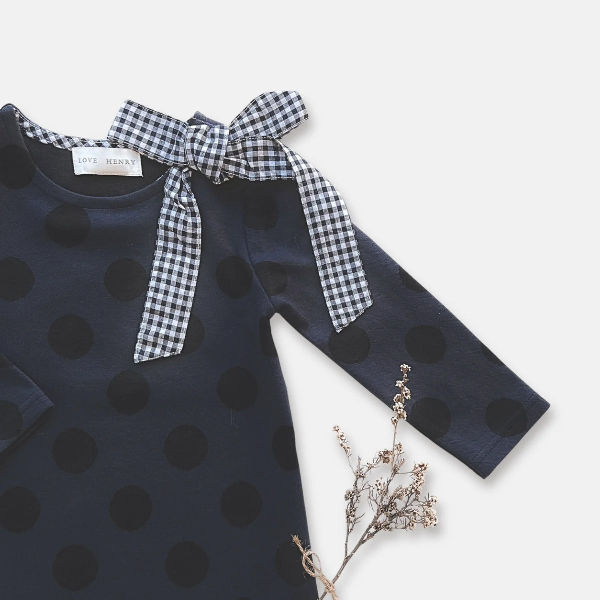 Love Henry Girl's Mary Dress. Navy blue dress with black polka dots and checkered bow on a light background.