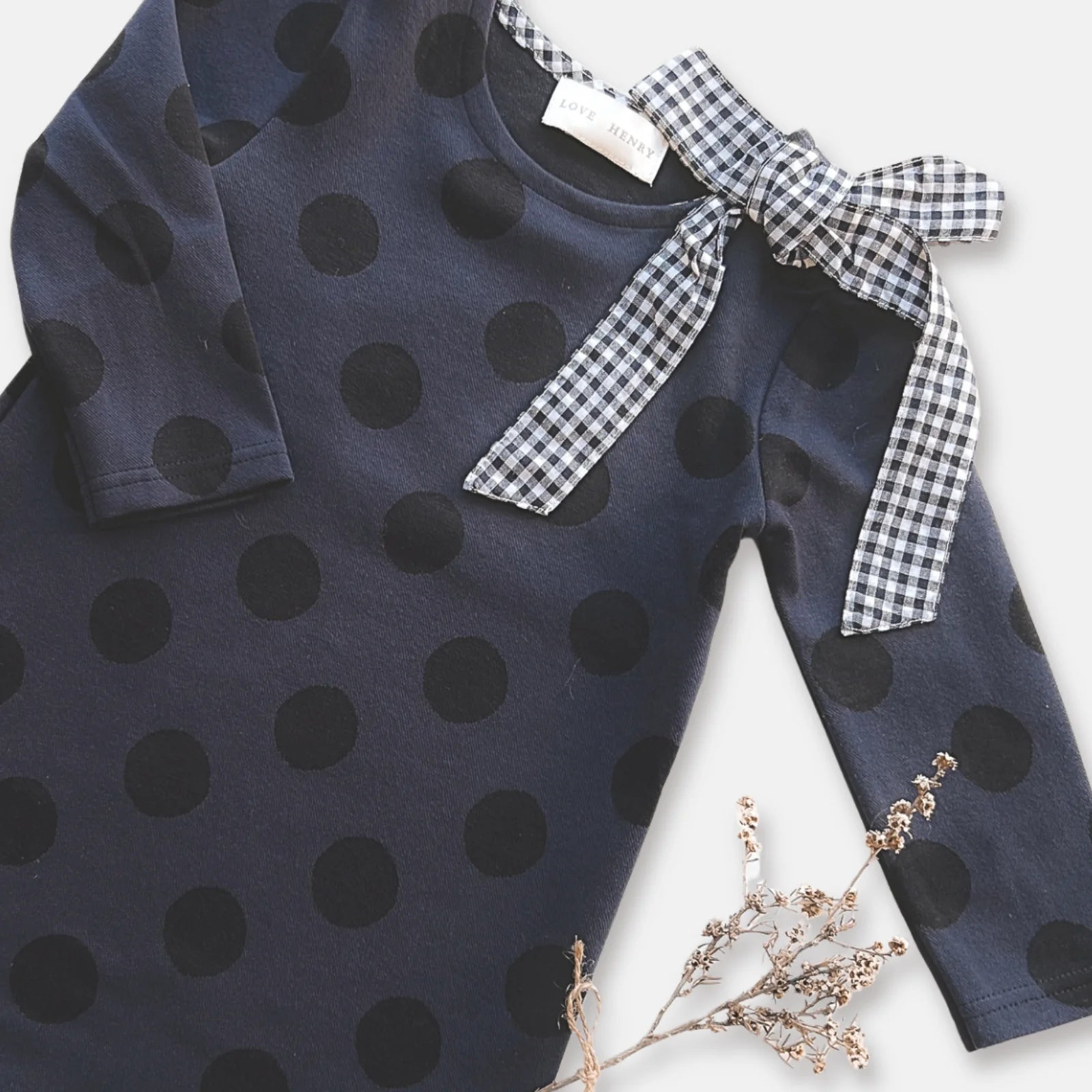 Love Henry Girl's Mary Dress. Navy polka dot dress with a bow on a white background