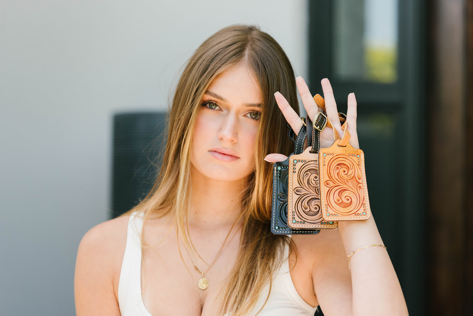 Woman holding three leather keychains in front of a neutral background