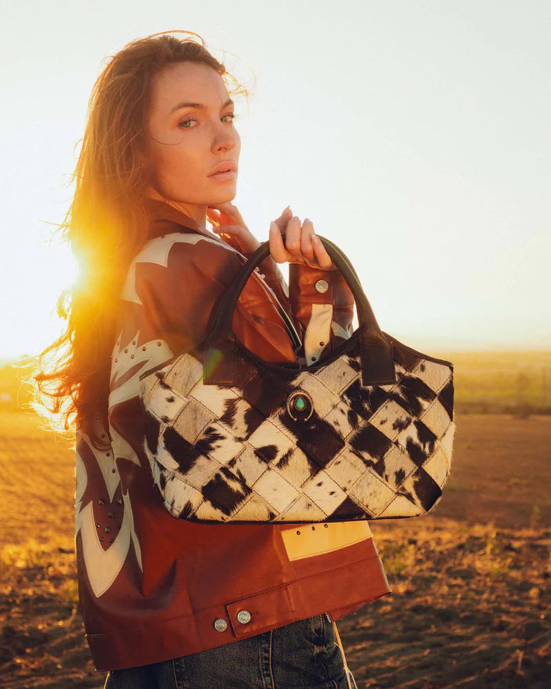Woman holding a patterned handbag in a field with sunset lighting
