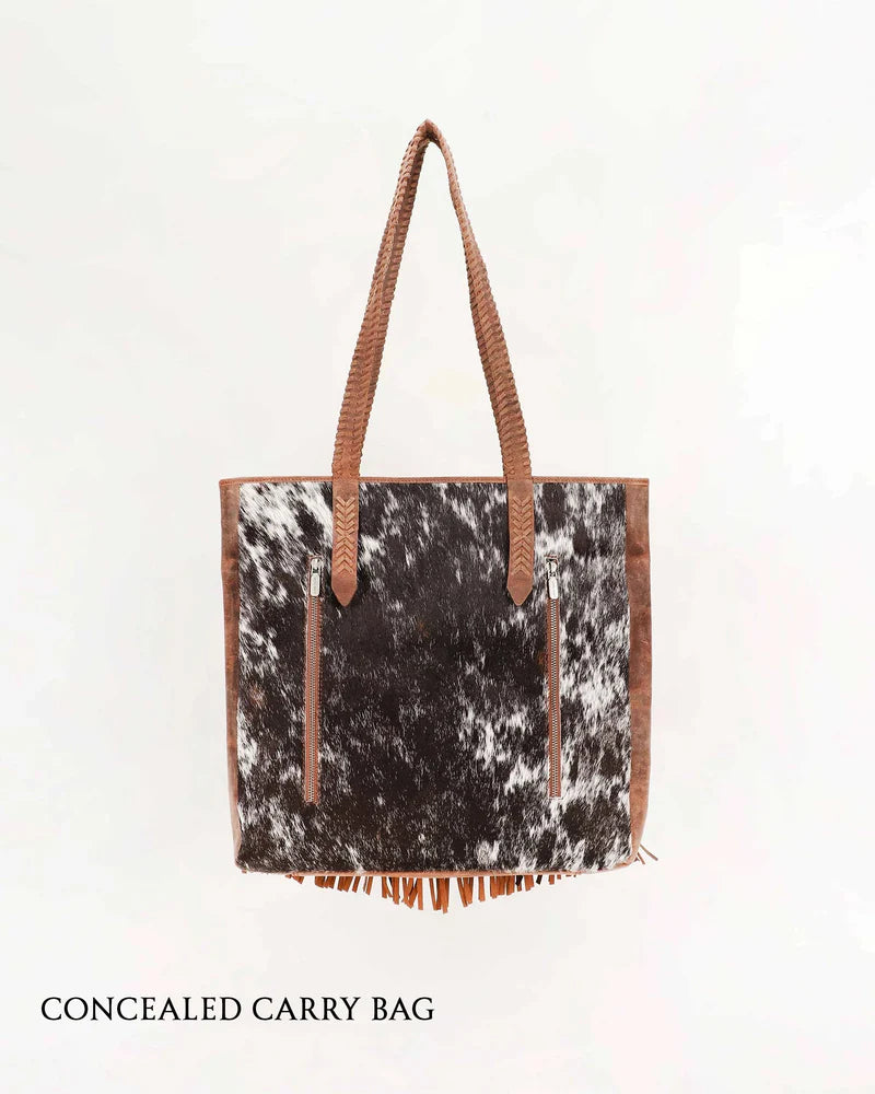 Loyal West Hide And Fringe Large Cowhide Western Handbag. Concealed carry bag with cowhide pattern and brown handles on a white background
