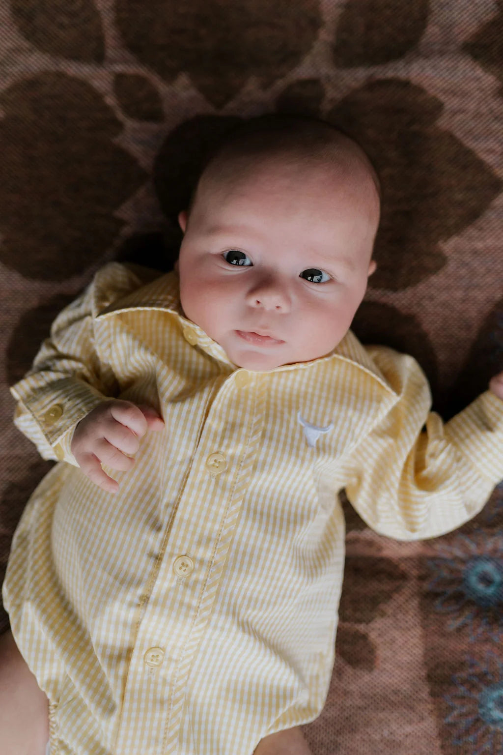 Baby wearing a yellow outfit lying on a patterned rug