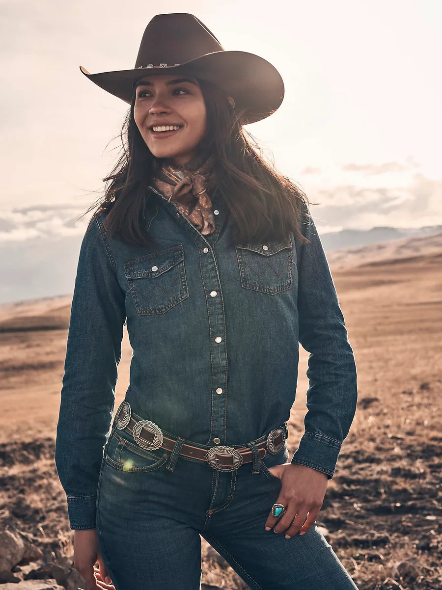 Wrangler Women's Classic Fit Denim L/S Western Shirt. Woman wearing a cowboy hat and denim shirt in a desert landscape