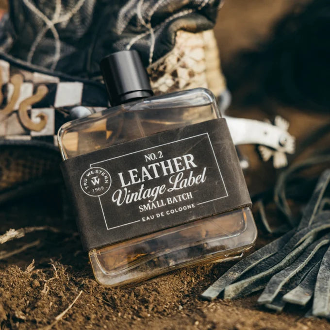 Bottle of 'Leather Vintage Label' cologne with leather gloves and a patterned fabric in the background