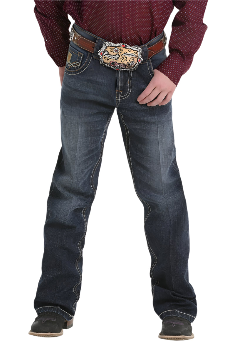 Cinch Boy&#39;s Relaxed Fit Jean. A boy standing straight, wearing a relaxed fit pair of blue jeans and a red shirt, with a decorative belt and buckle.