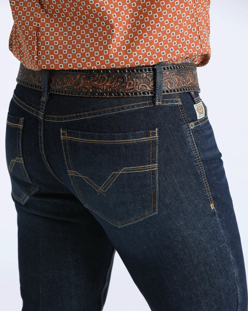 Person wearing dark blue jeans with a patterned shirt and belt on a white background