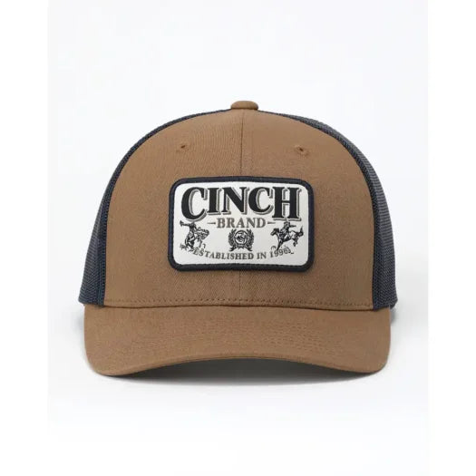 A tan and navy blue trucker hat with a rectangular embroidered patch on the front that reads 'CINCH BRAND ESTABLISHED IN 1865'.