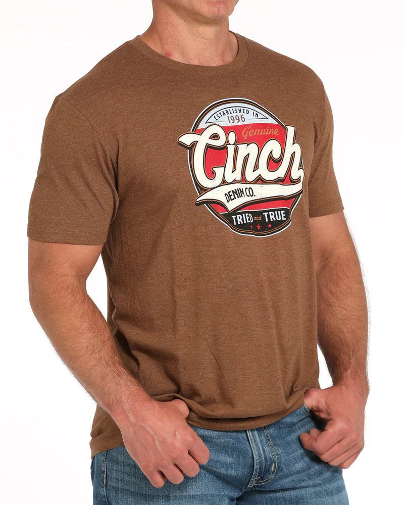 Cinch Men's Graphic T-Shirt. Man wearing a brown t-shirt with a 'Ginch' logo on a white background