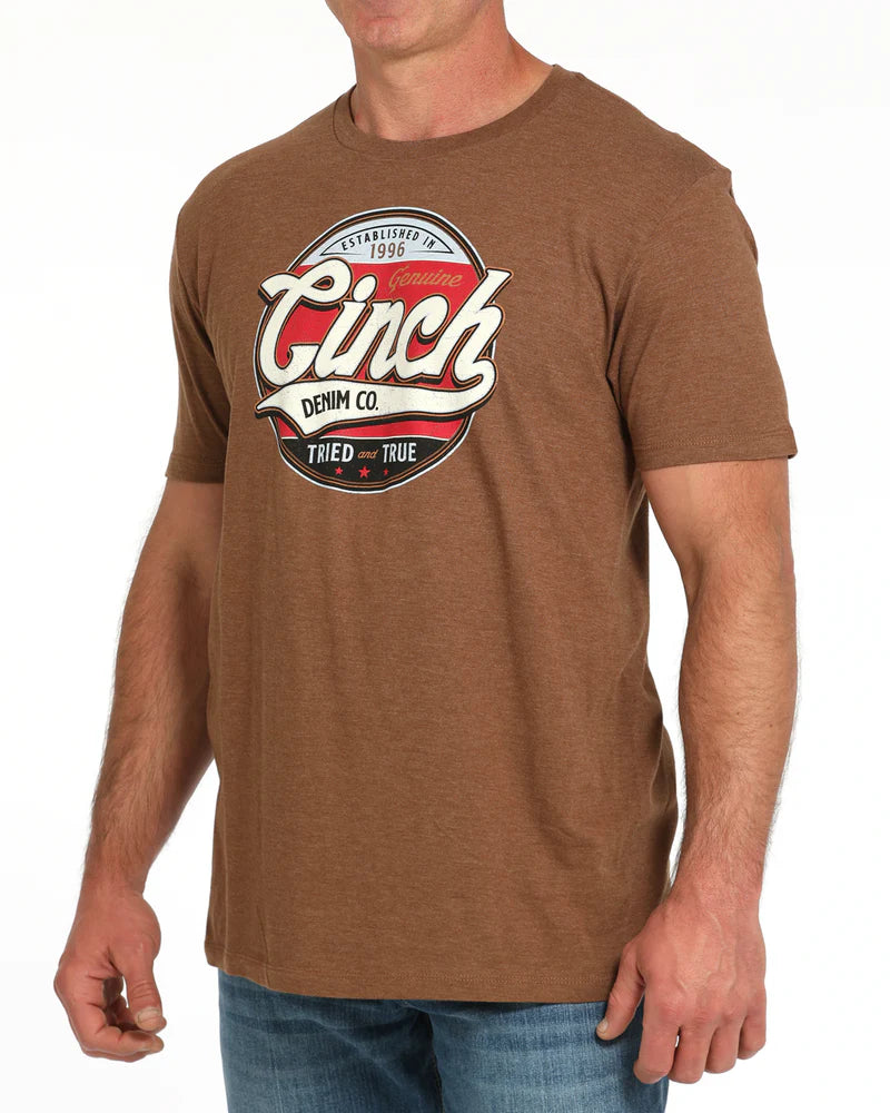 Cinch Men's Graphic T-Shirt. Brown t-shirt with Cinch Denim Co logo worn by a person on a white background