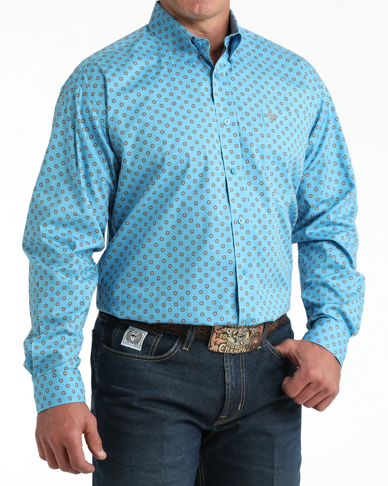Man wearing a light blue patterned shirt and dark jeans on a white background