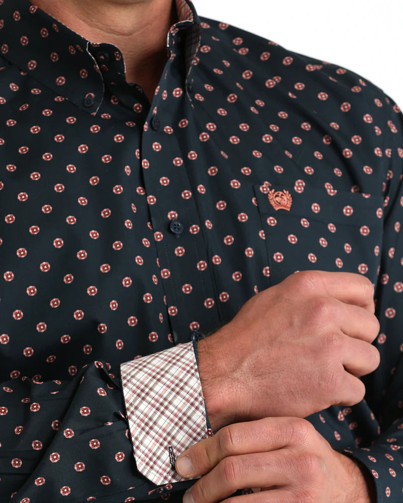 Close-up of a person wearing a dark patterned shirt with a visible brand logo.