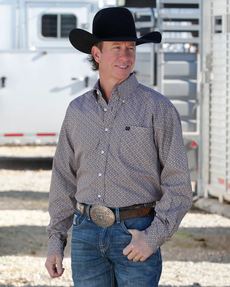 Man wearing a cowboy hat and patterned shirt standing in front of a trailer.