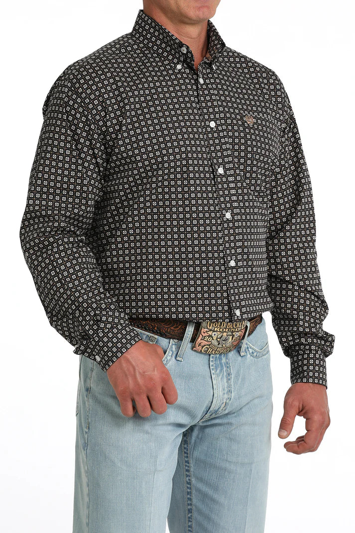 Man wearing a patterned black and white shirt with light blue jeans on a white background