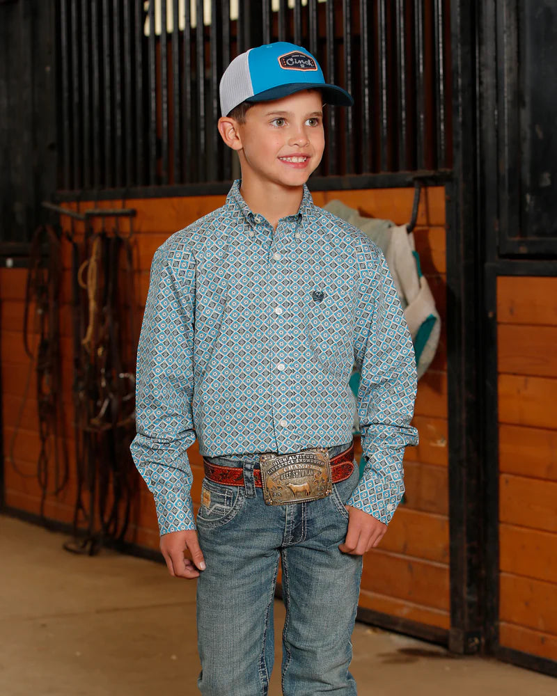 Cinch Boy's Geometric Print L/S Western Shirt. Young boy in a patterned shirt and jeans standing in a stable.