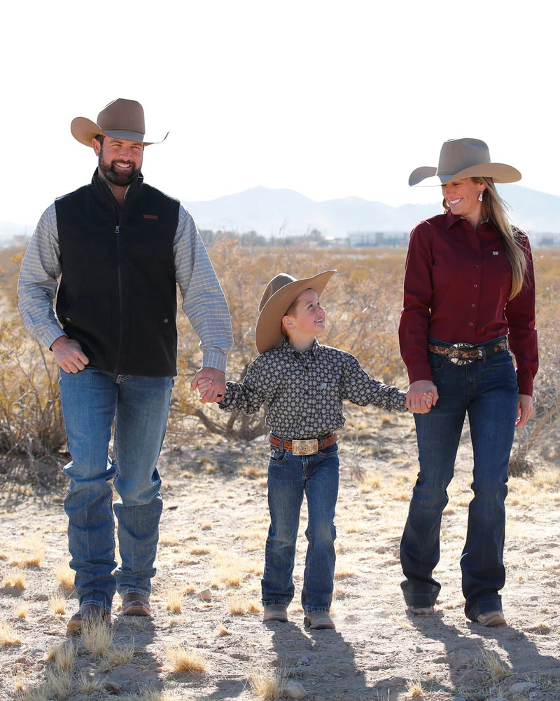 Family of three, including a man, woman, and child, wearing cowboy hats and boots in a desert landscape.